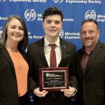 A woman and two men stand together. The man in the middle is holding an award for Outstanding Senior Engineering Student.