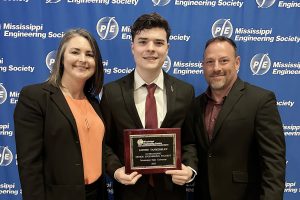 A woman and two men stand together. The man in the middle is holding an award for Outstanding Senior Engineering Student.